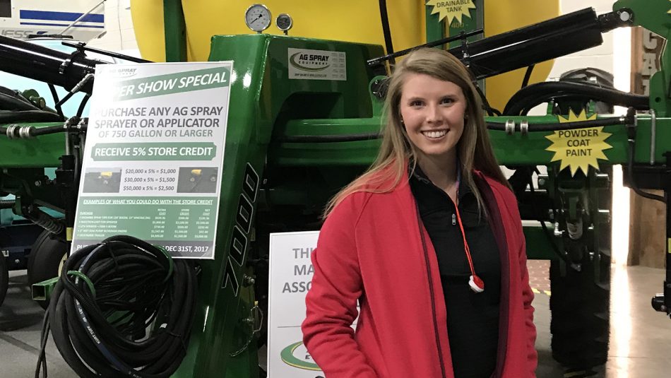 Katelyn Thomas stands in front of an ag sprayer