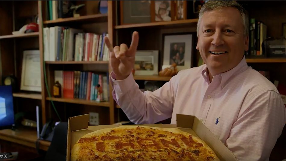 Dean Linton does the wolf hand gesture while holding a pizza
