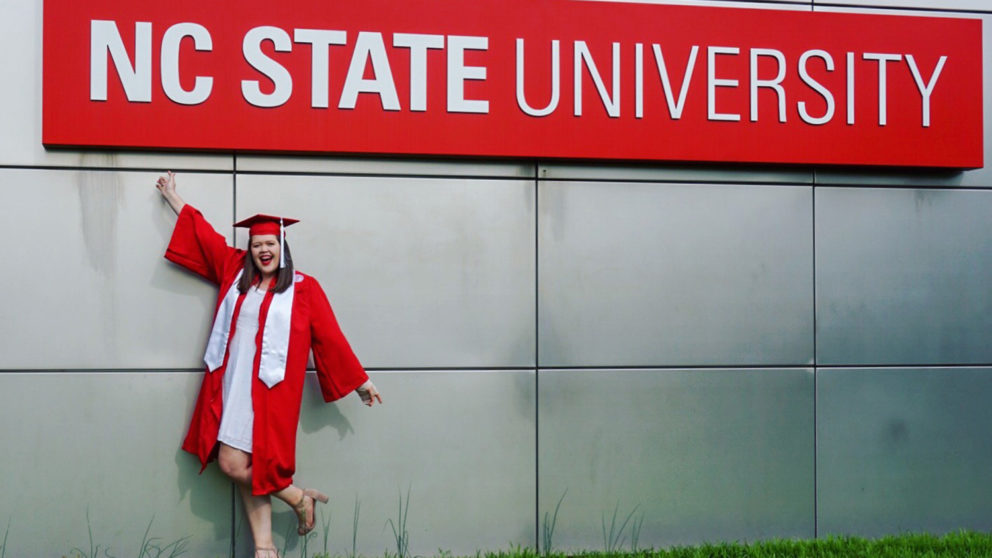 Ellison Lambert poses in front of the NC State sign in cap and gown