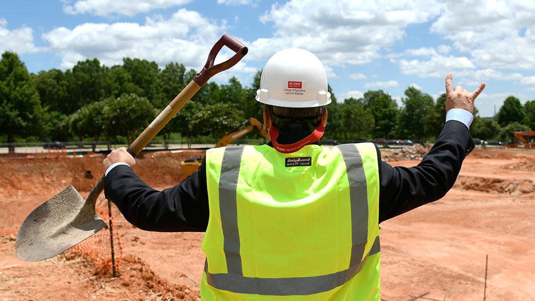 a man in construction gear doing wolf hands while overlooking construction site