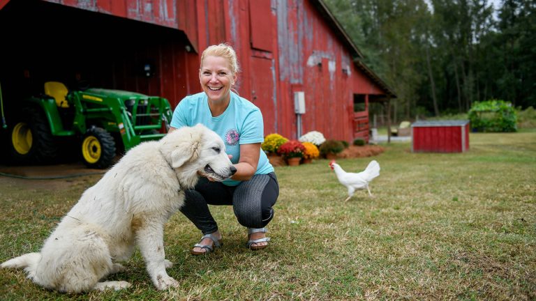 Roxanne Reed with her working dog and a chicken outside of a barn