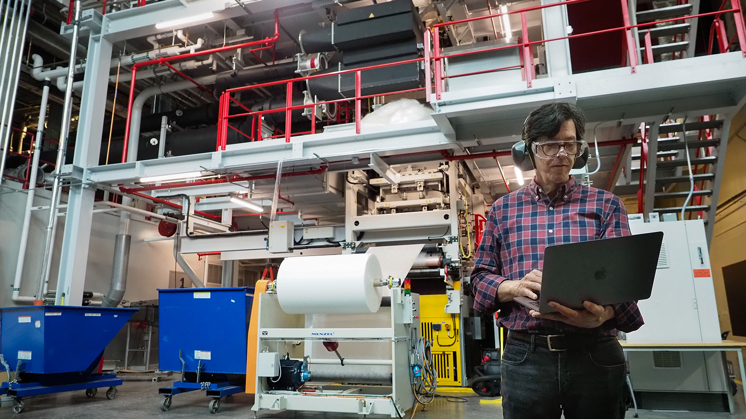a member of the nonwovens institute stands in front of machinery holding a laptop