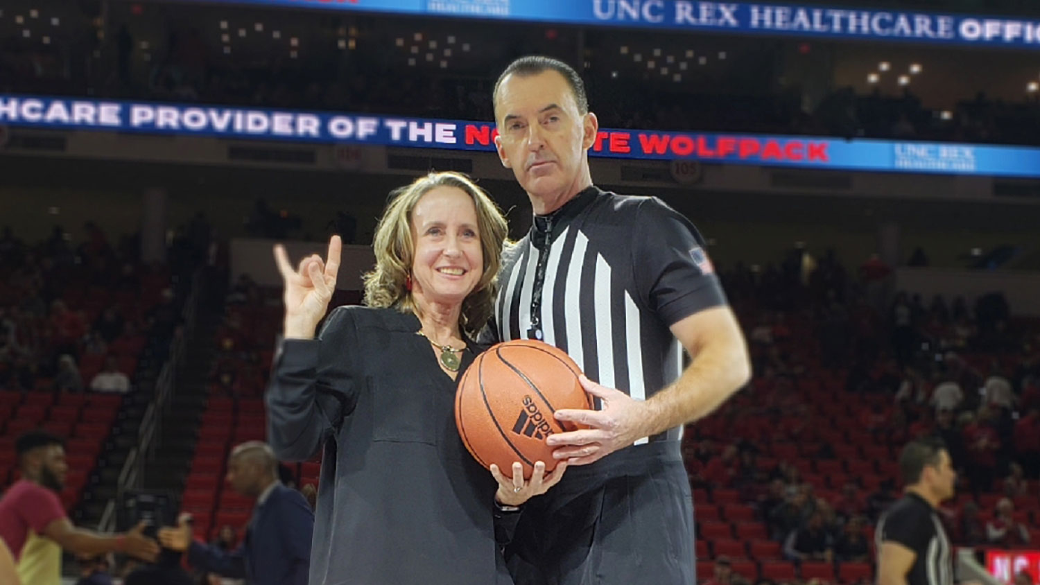 Linda Butler with does the wolfie on the basketball court with a referee