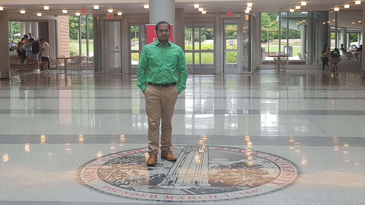 Samit Chakraborty standing by the NC State seal in Talley Student Union
