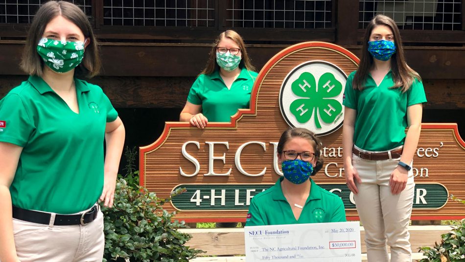 4-H students wearing face coverings pose with a check outside of the 4-H learning center