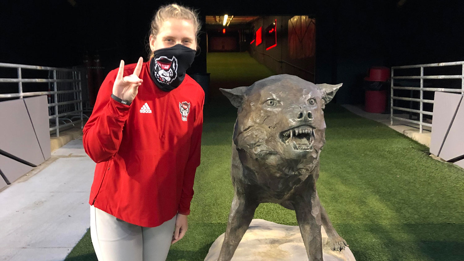 Crista Bain holding up the wolf ears symbol next to a wolf statue