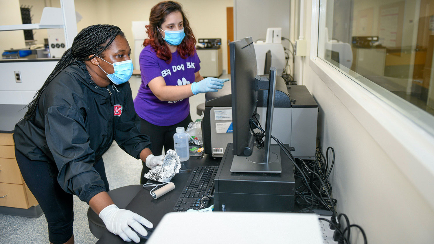 Two people in face coverings work on a computer