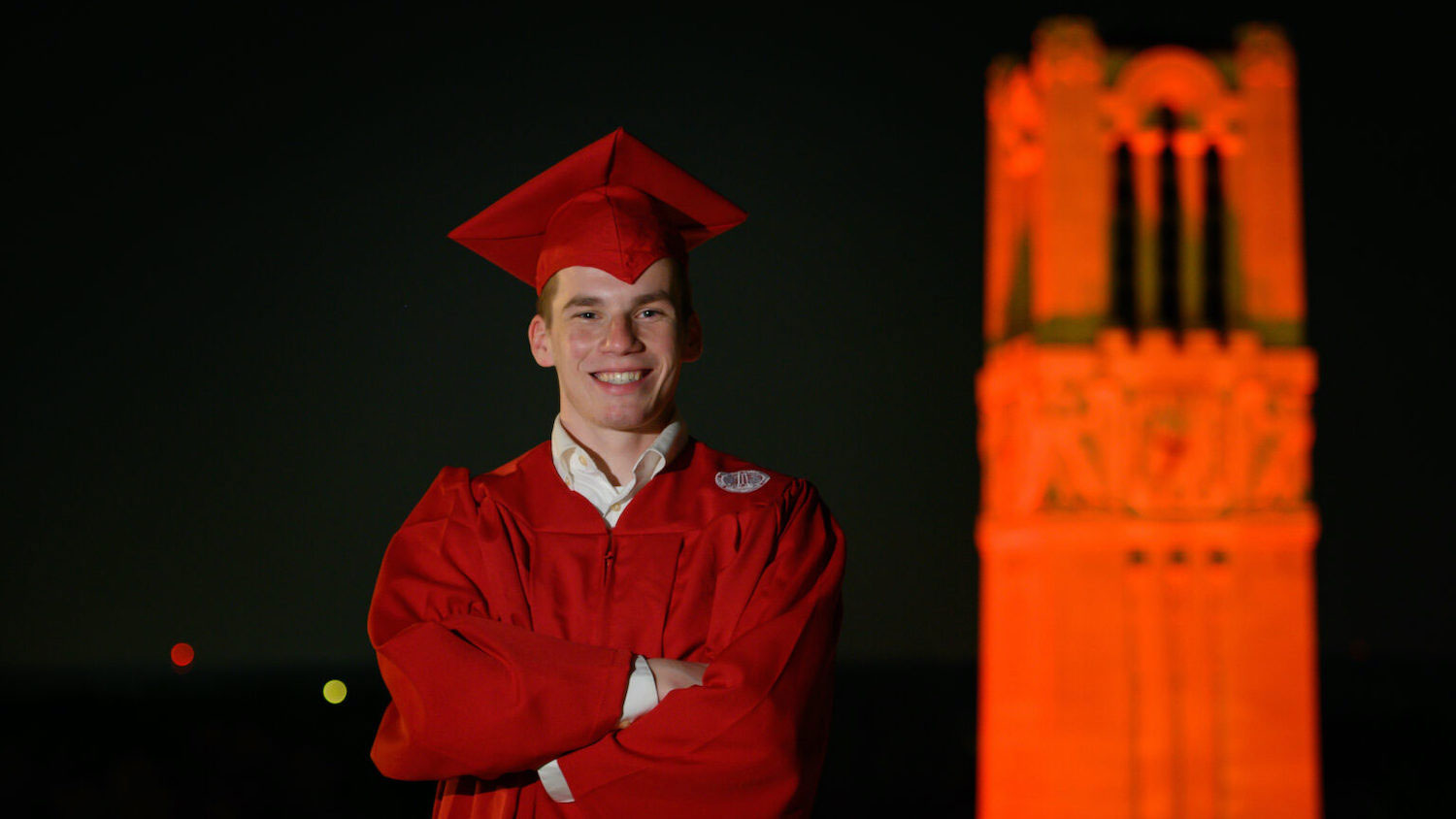 Jush Guter in his graduation gown in front of the belltower, which is lit red