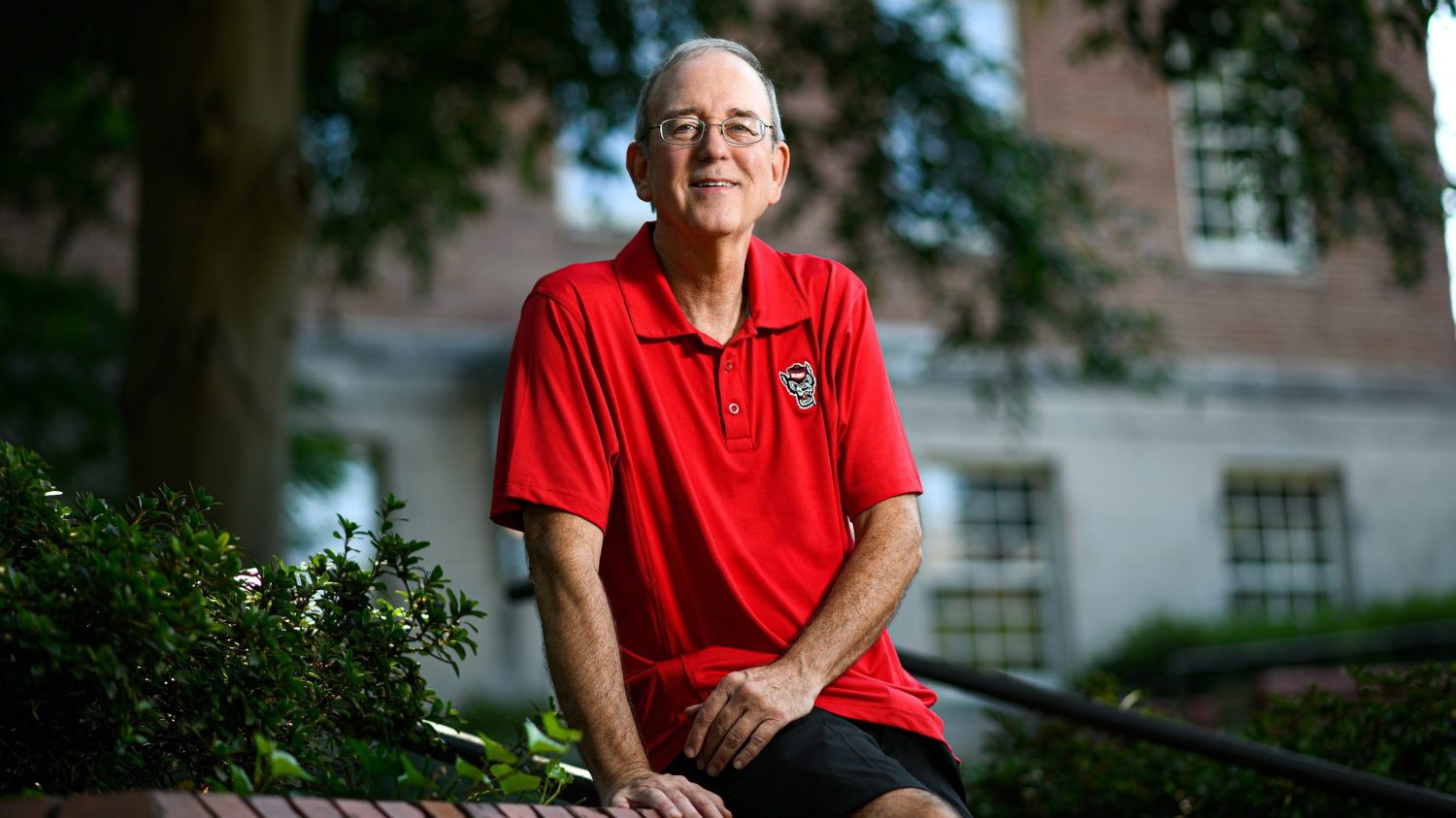 William O'Brien sits on a wall at NC State's campus in a red Wolfpack polo.