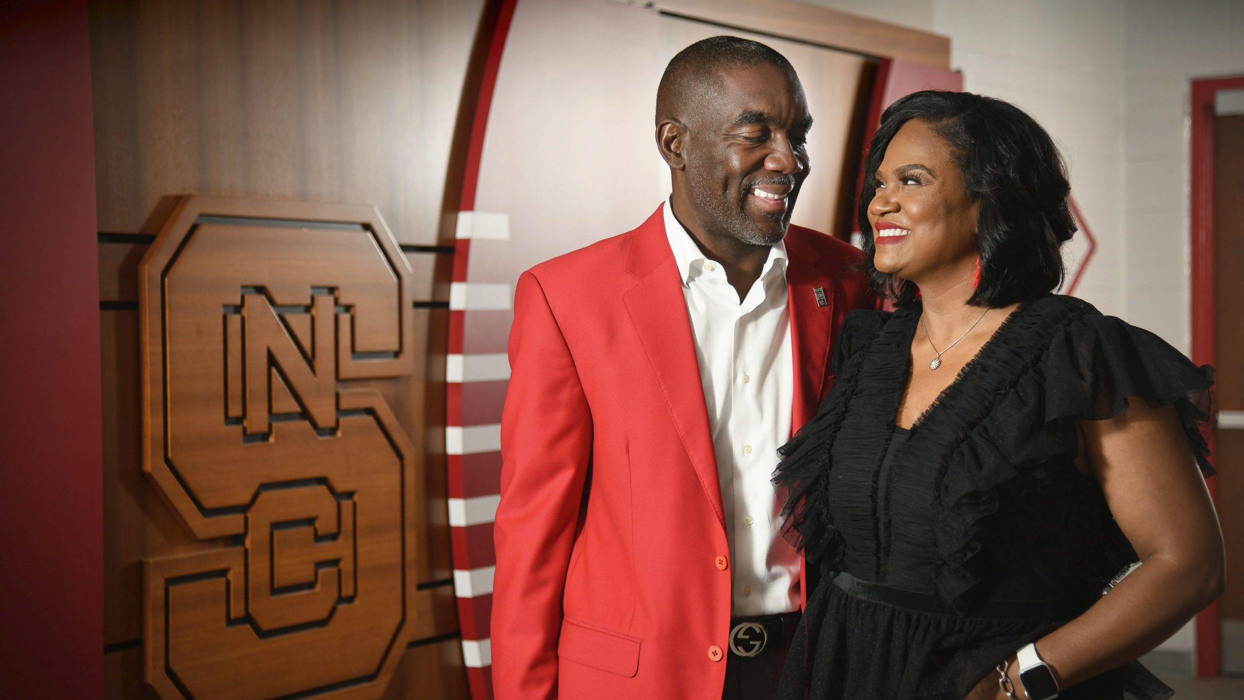 Dewayne and Adama Washington smiling at each other in front of the N.C. State logo.