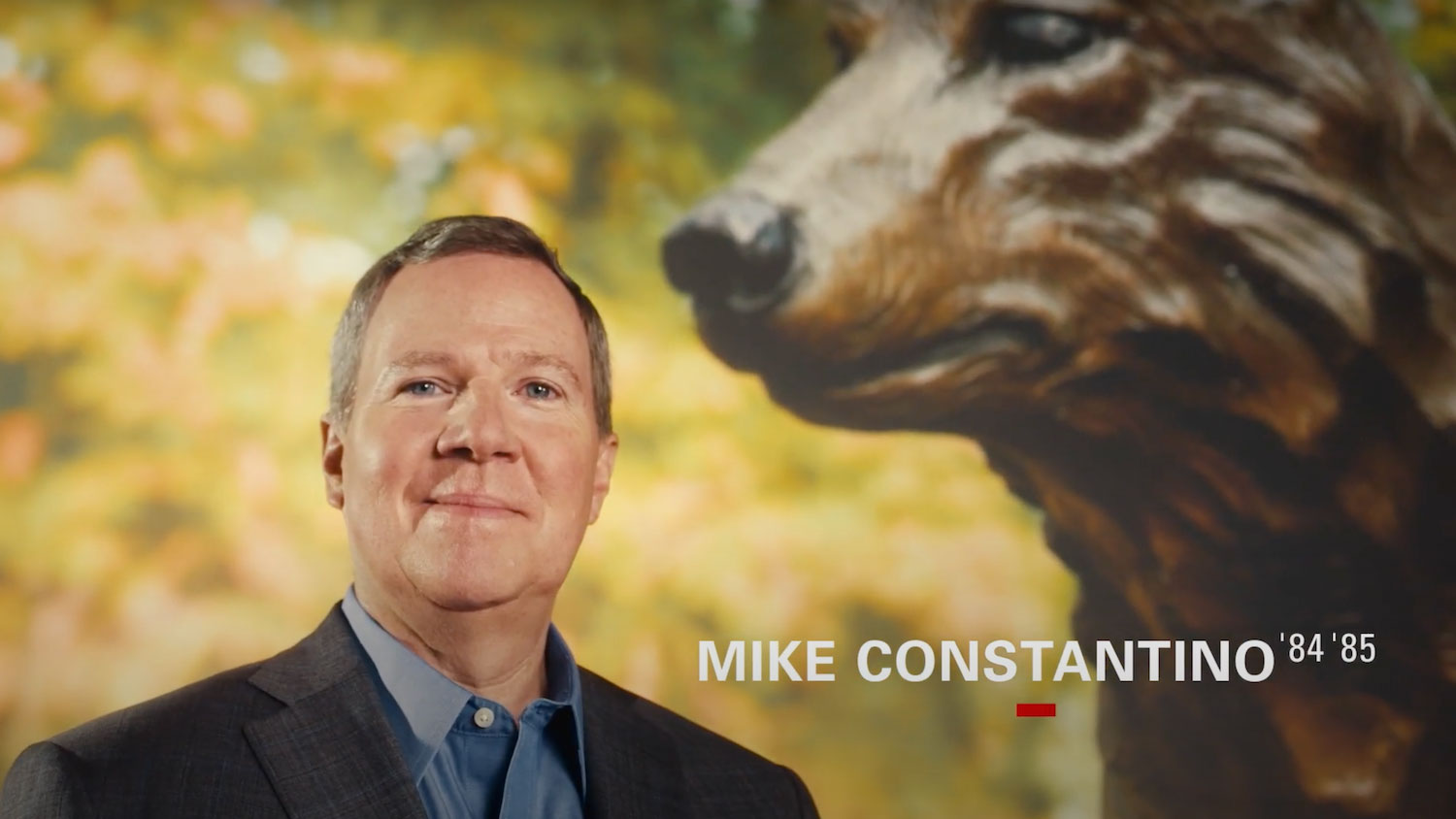 Mike Constantino in front of a background of a wolf statue and his name and graduation years listed