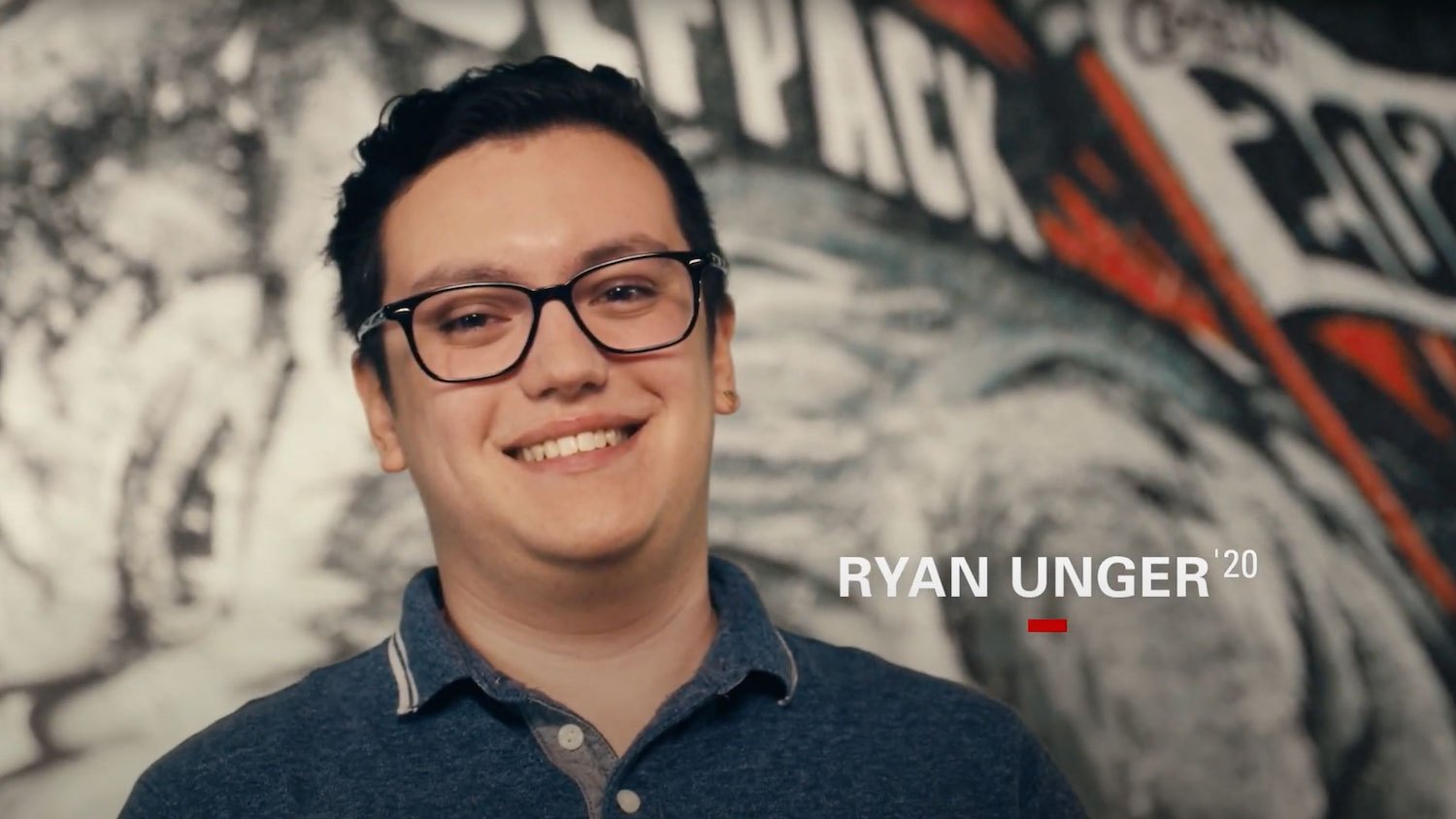 Ryan Unger smiling to the camera in front of wolfpack themed art.