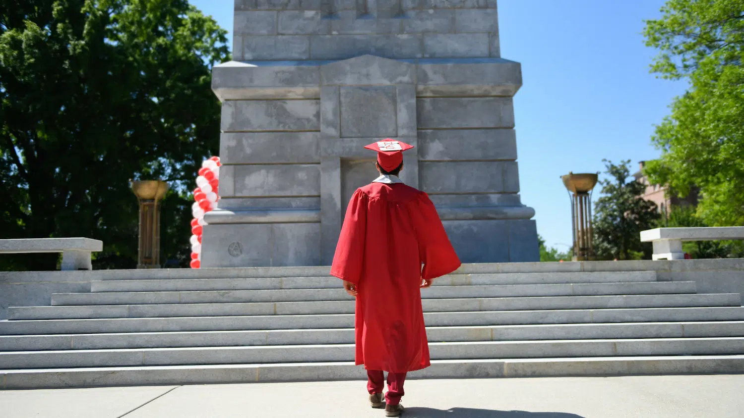 Graduate in cap and gown walking toward the Memorial Belltower
