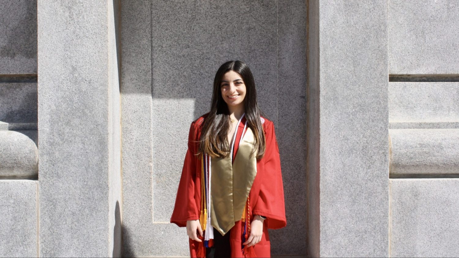 Loujain Al Samara posing a smile in front of the Belltower in her cap and gown.