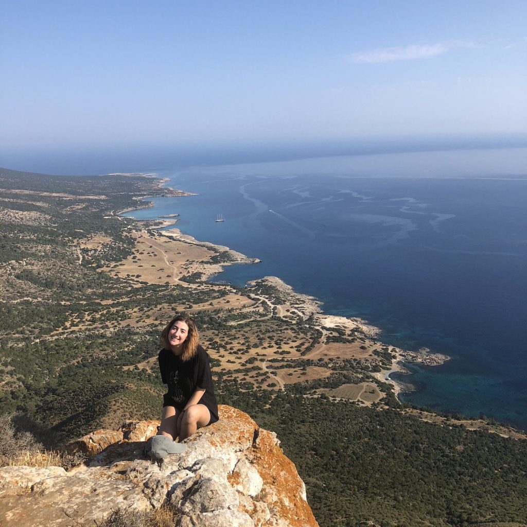 Lara sitting at the edge of a mountain during her trip to Cyprus in 2019.