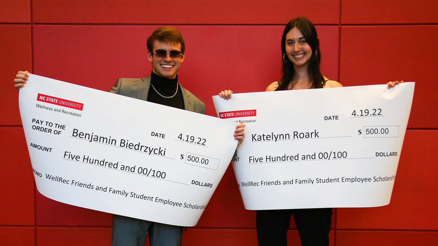 Ben Biedrzycki and Katelynn Roark hold giant checks from Wellness and Recreation