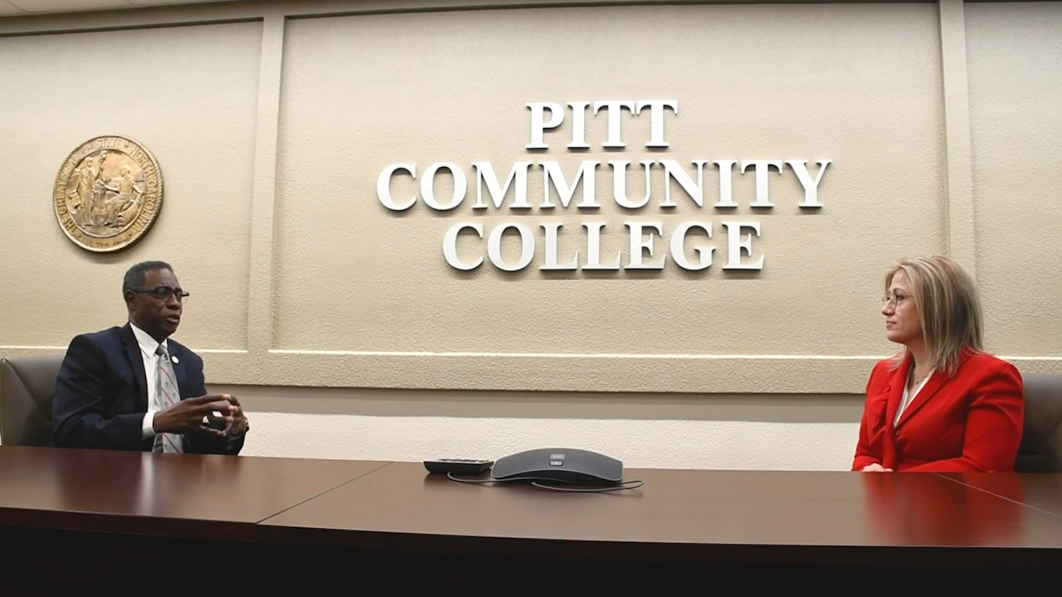 Lawrence Rouse and Monica Clark at a table in front of a Pitt Community College sign