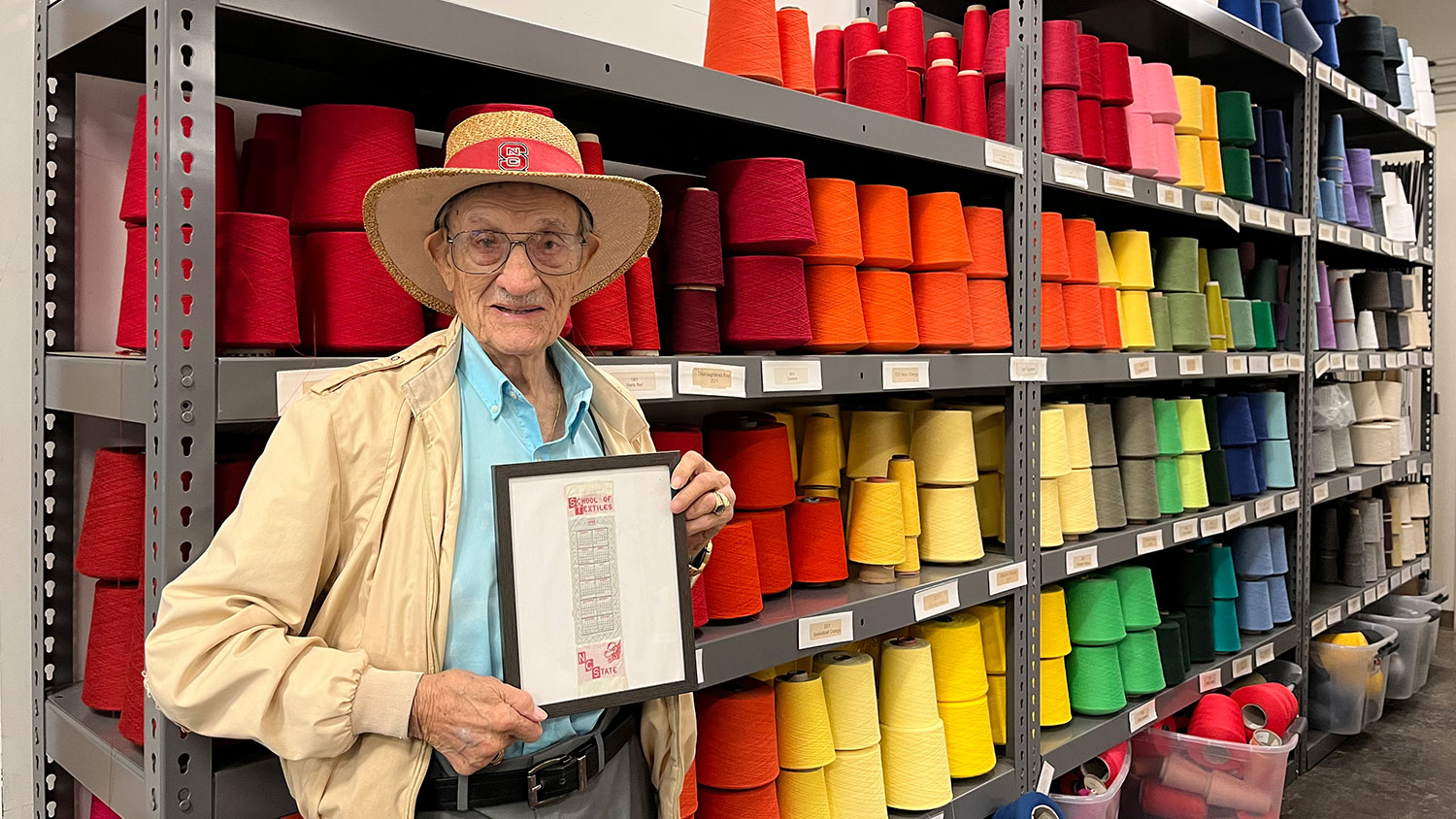 Willie Bowen and his first Wilson College of Textiles bookmark in front of shelves of different colored threads