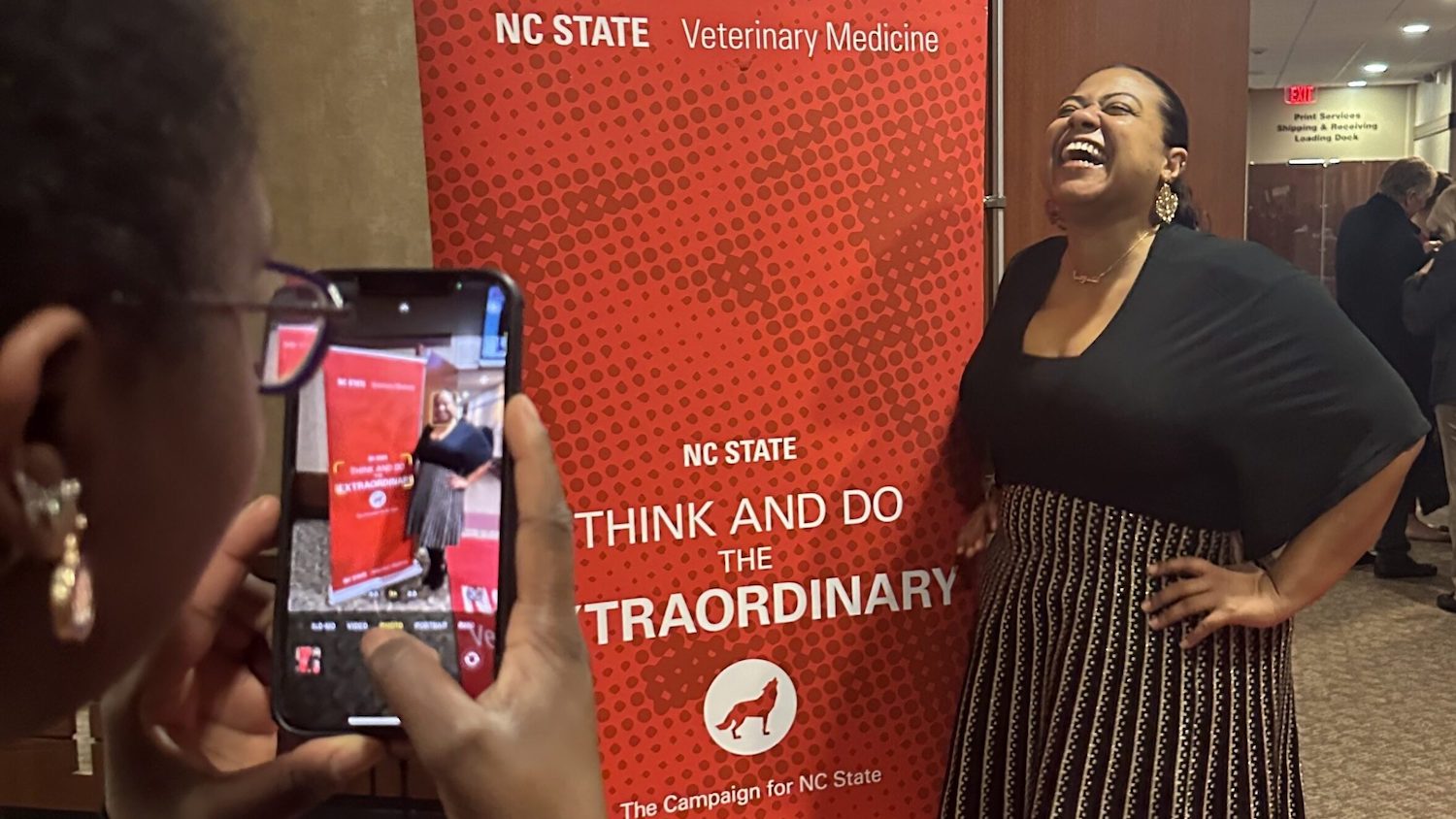 An NC State donor poses for a photo beside a university banner.