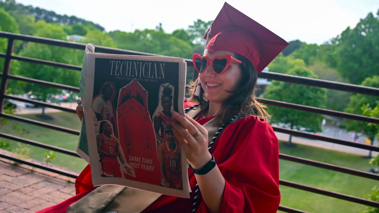 Jameson Wolf in her cap and gown reading an issue of the Technician