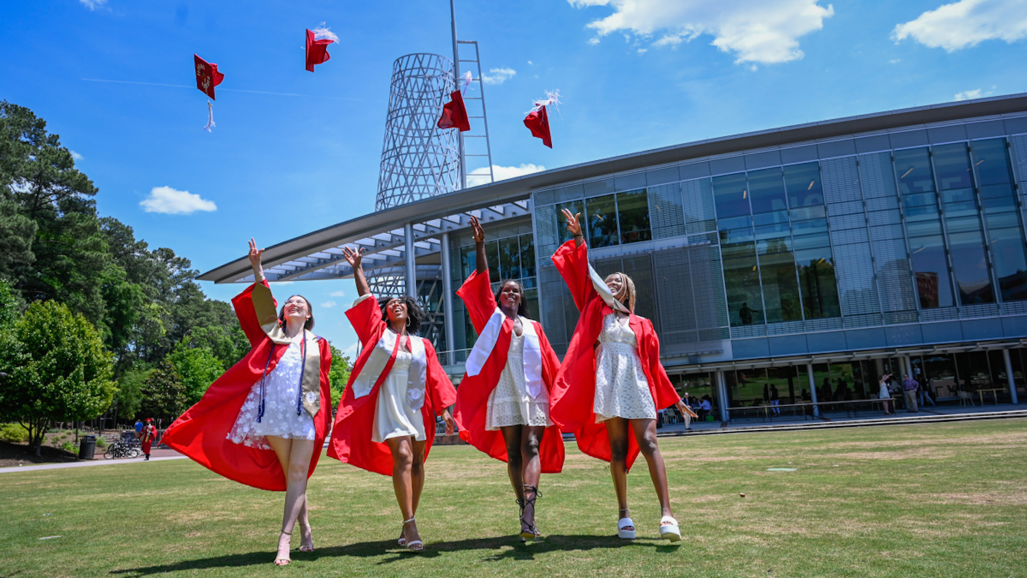 Four women in graduation gowns throwing their caps in front of Talley Student Union.