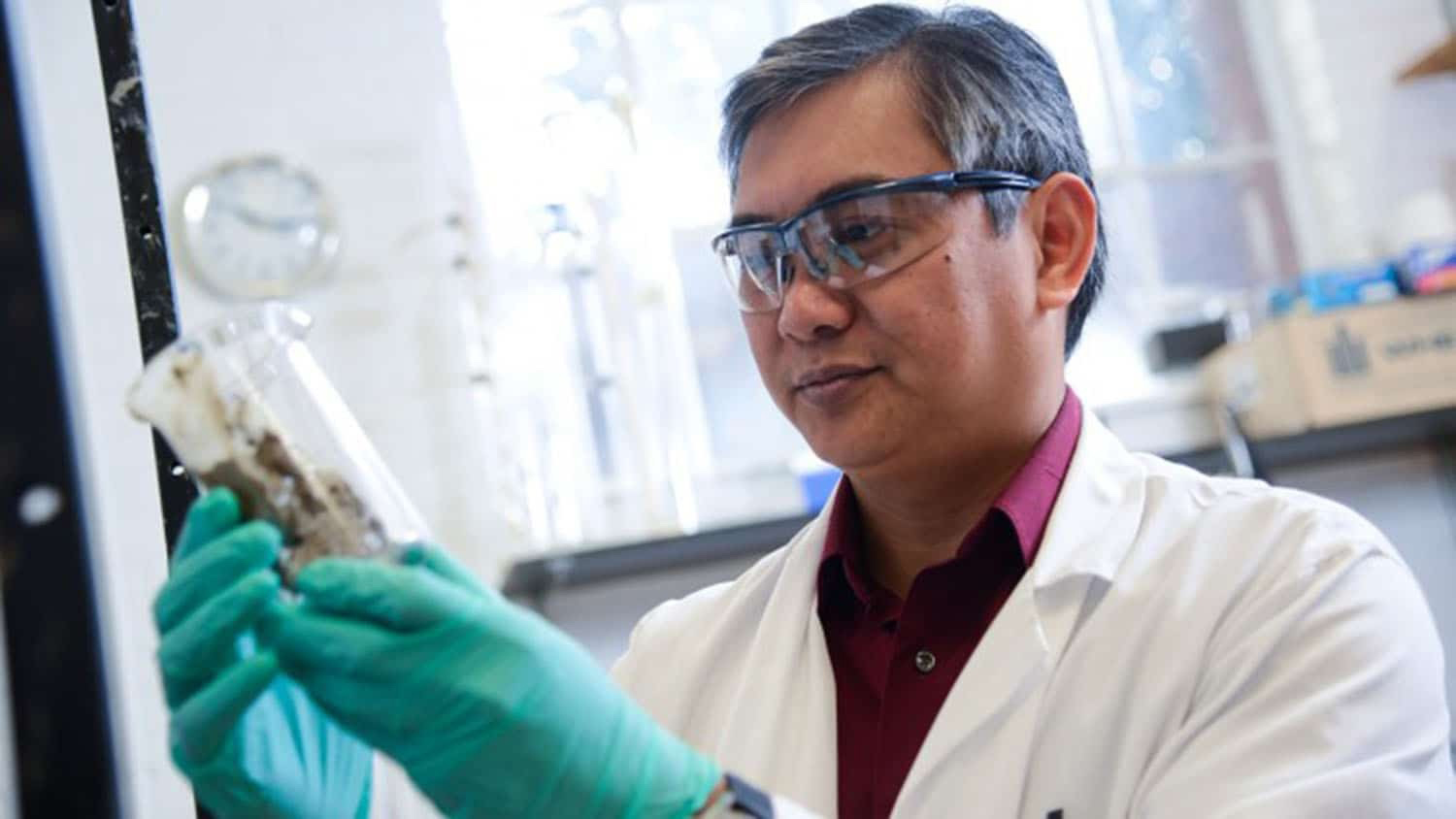 Francis de los Reyes III holding a beaker in a laboratory.