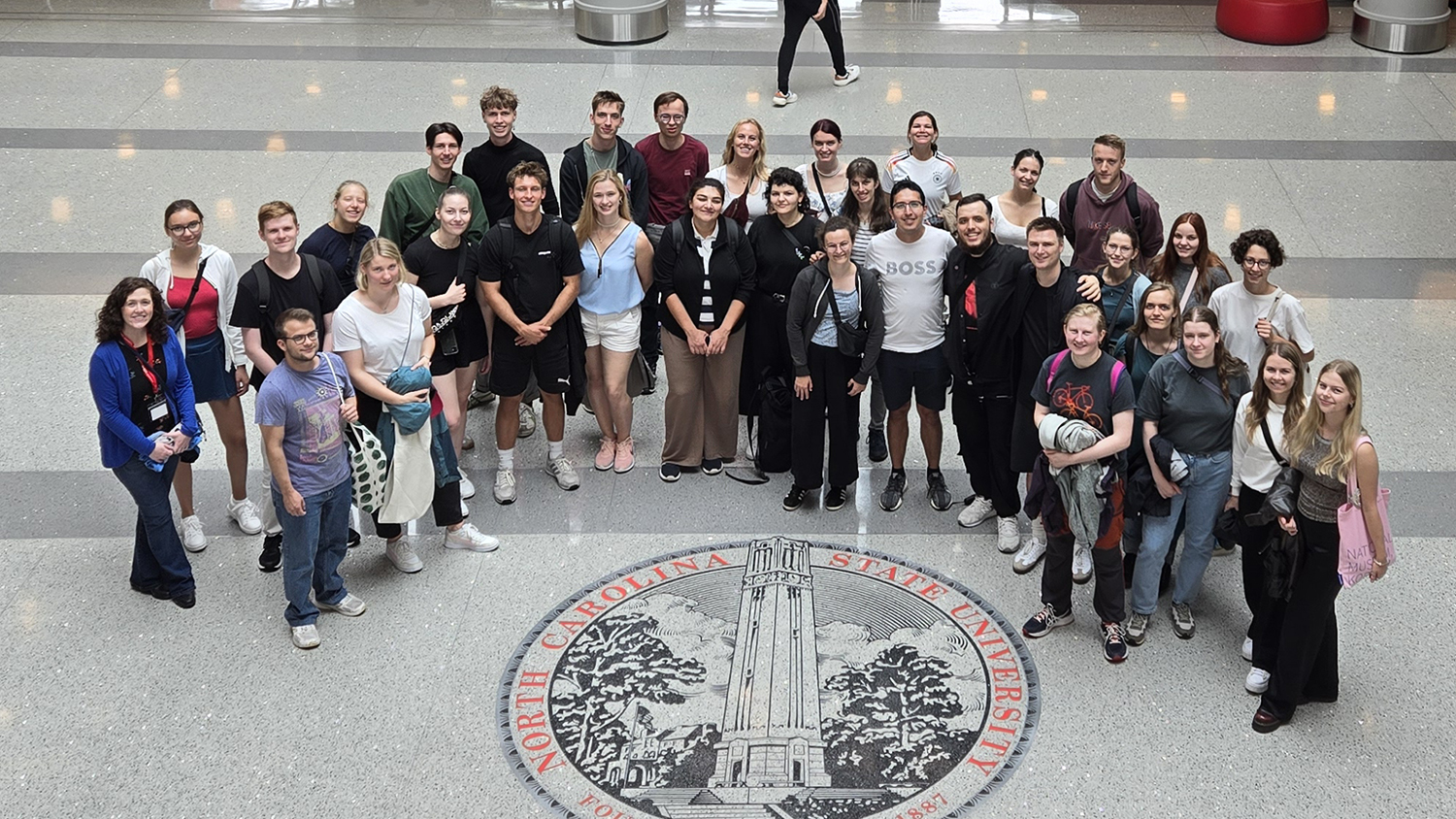 Members of the German-American Fulbright Commission standing around the NC State symbol in Talley Student Union.