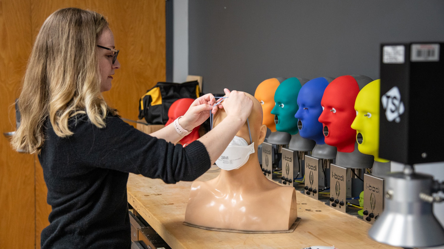 Melissa Armistead putting a mask on a mannequin head.