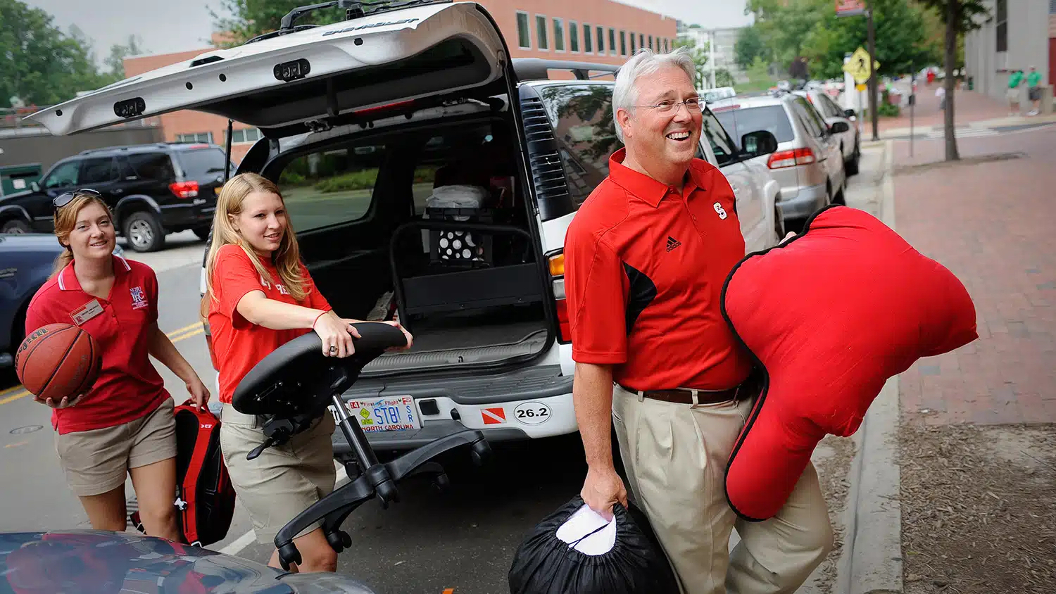 Chancellor Woodson and two students helping carry items during move-in weekend.