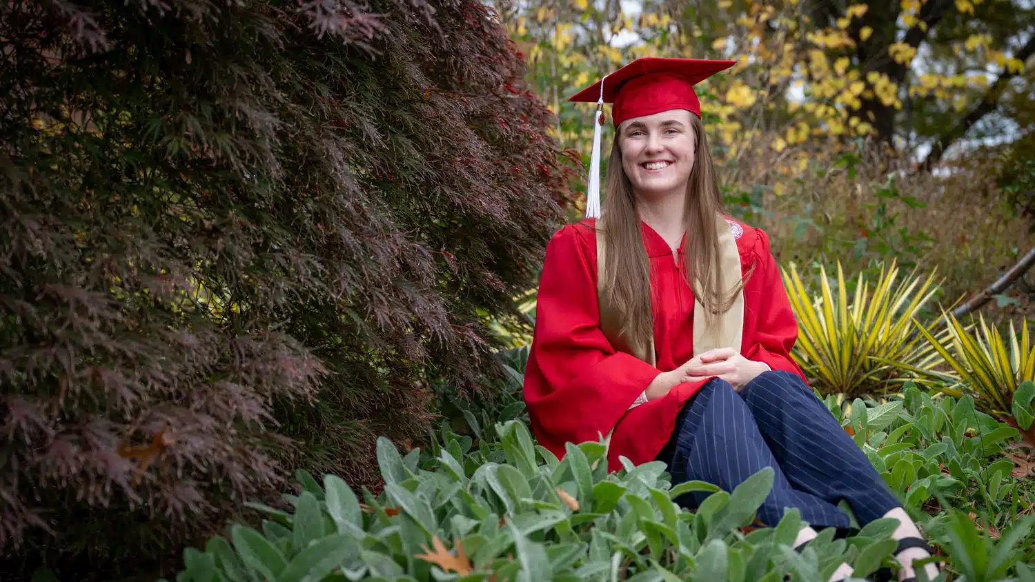 Graduating student posing for a photo next to a tree