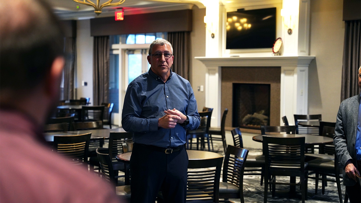 Basil Hassan standing in a large room talking to people just outside of the photo.
