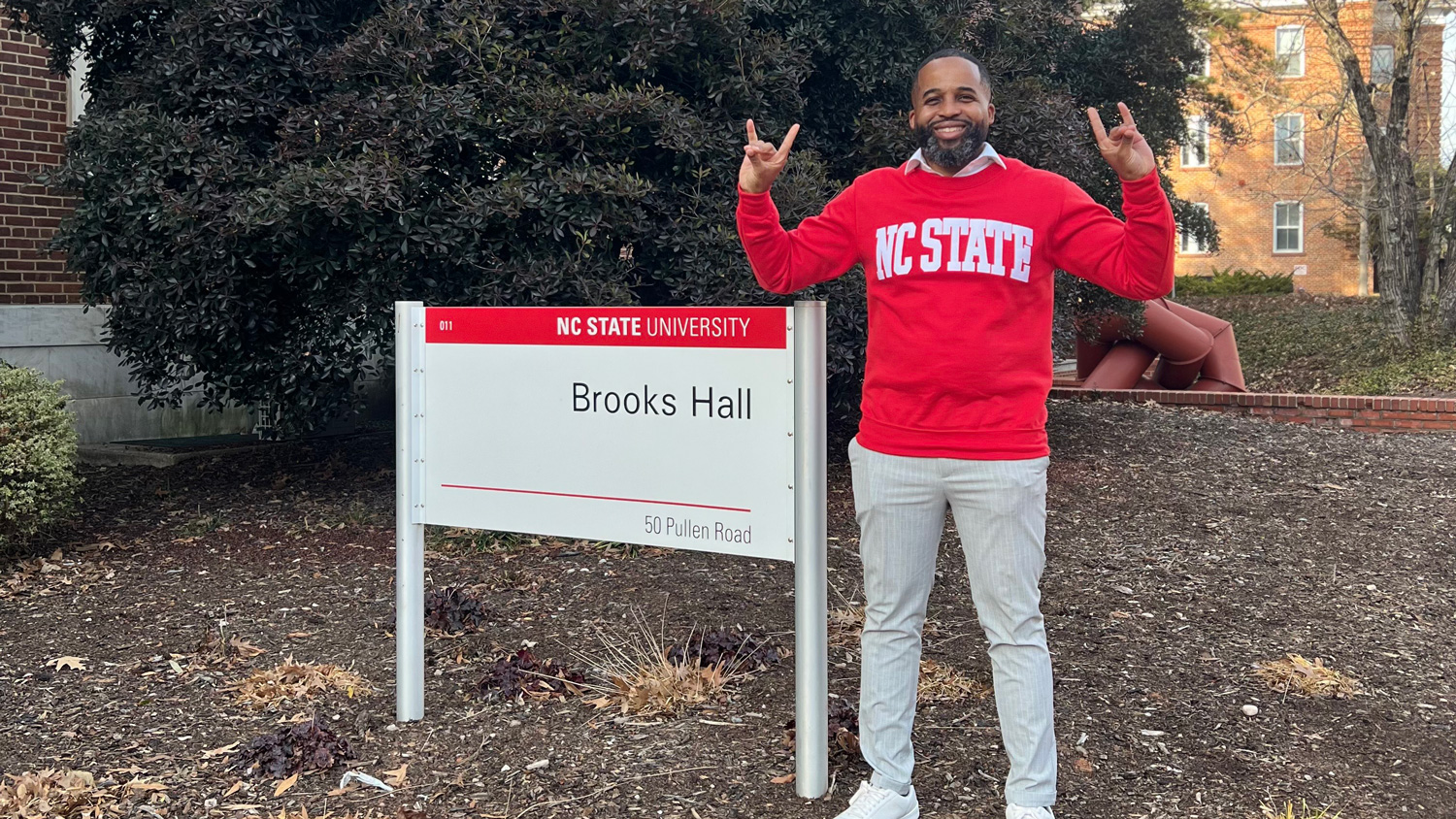 Demarcus Williams holding up the wolfie hand sign next to a Brooks Hall sign
