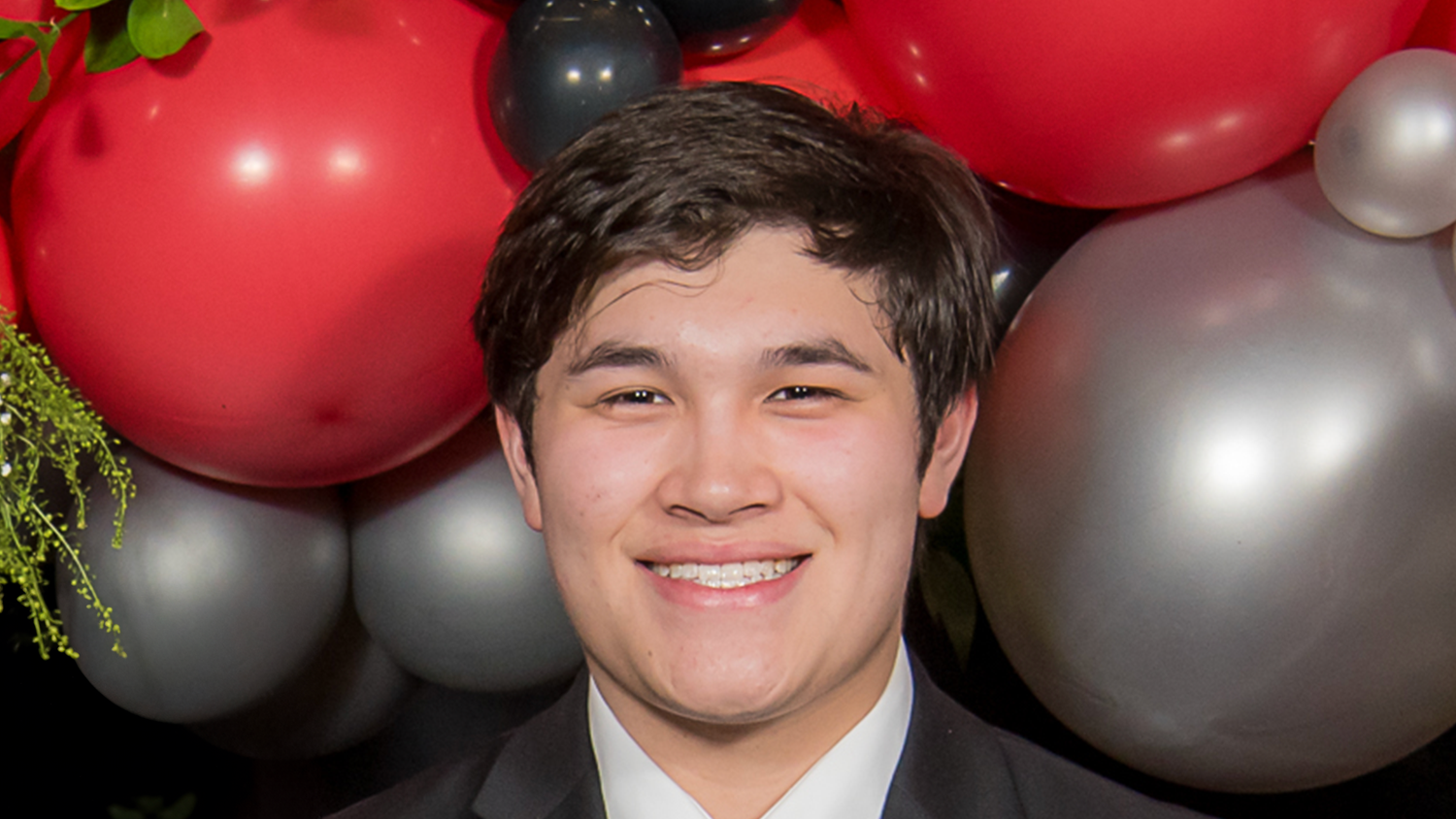 Thomas Nguyen smiling in front of a background of balloons