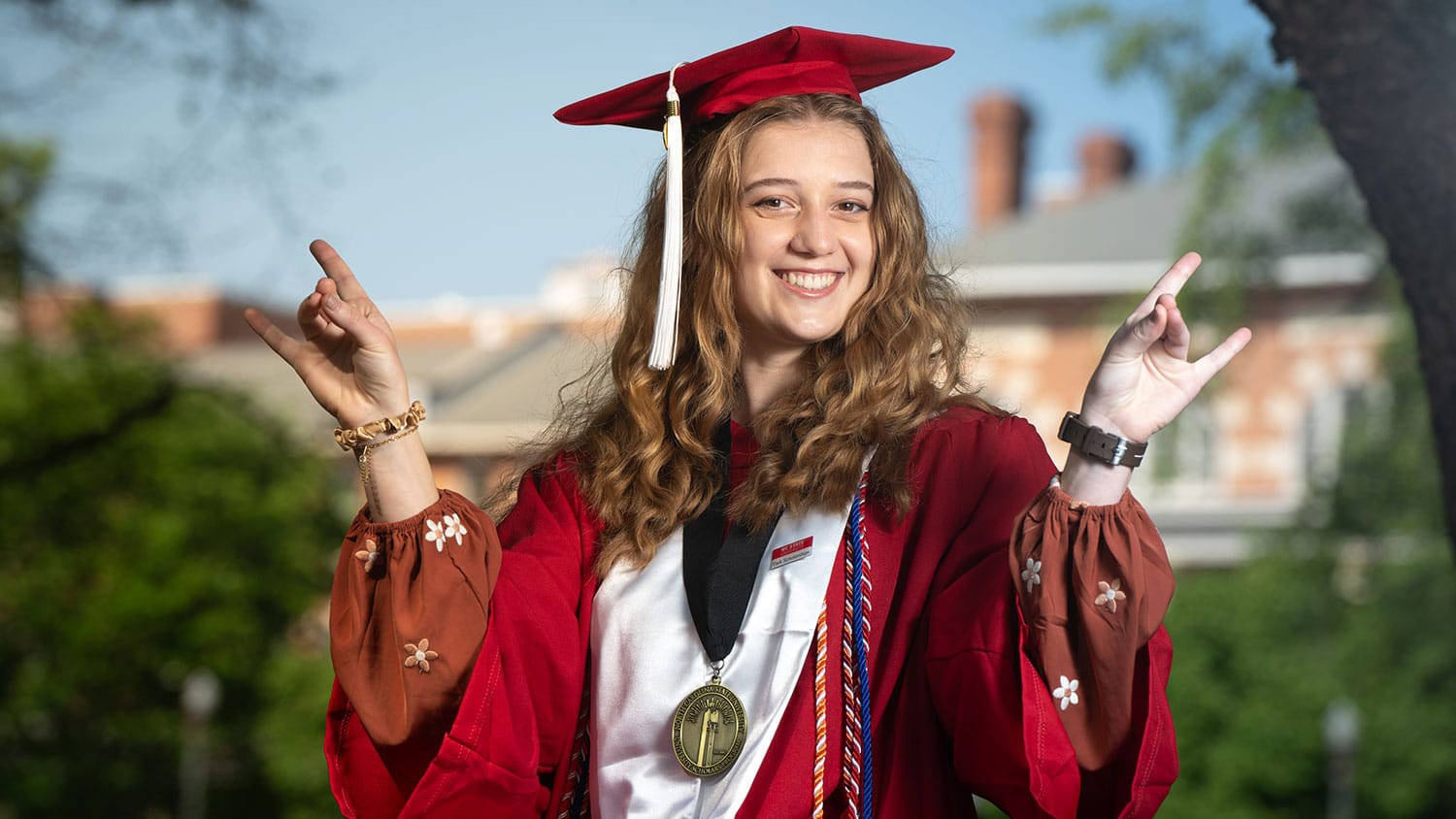 Emily Boldor in her graduation cap and gown holding up the wolfie hand sign.