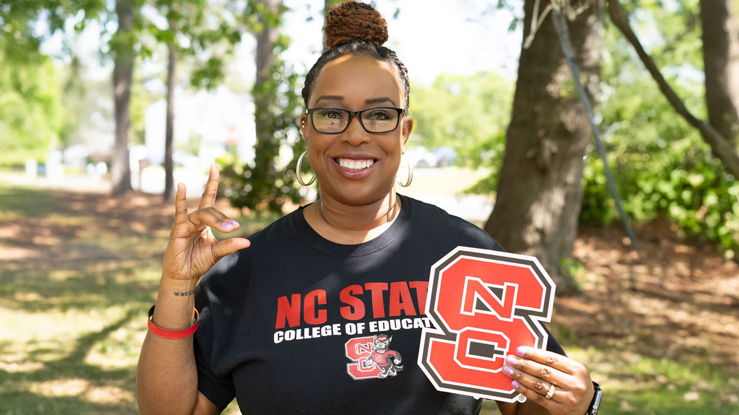 Kimberly Sutton holding a "block S" NC State logo and a wolfie hand sign.