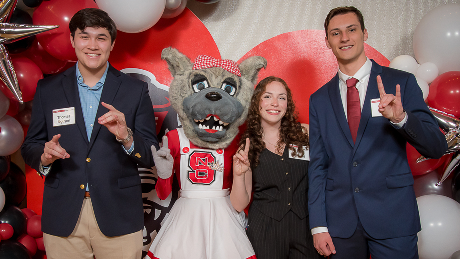 Three College of Education scholarship recipients holding up the wolfie hand sign with Ms. Wuf.